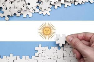 Die argentinische Flagge ist auf einem Tisch abgebildet, auf dem die menschliche Hand ein weißes Puzzle faltet foto