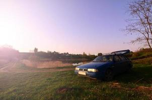 Ein blaues Auto vor dem Hintergrund einer rustikalen Landschaft mit einem wilden Zuckerrohrfeld und einem kleinen See. Die Familie kam in der Natur in der Nähe des Sees zur Ruhe foto