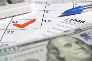 1040 individuelle Einkommensteuererklärung leer mit Dollarnoten, Taschenrechner und Stift auf Kalenderseite mit markiertem 15. April foto