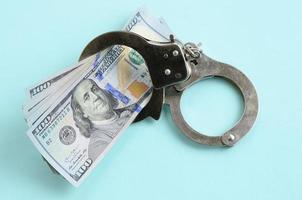 Silberne Polizeihandschellen und Hundertdollarscheine liegen auf hellblauem Hintergrund foto