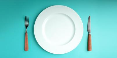 weißer leerer teller mit gabel und messer lag auf blauem tischhintergrund. Nahrungsmittelknappheit, Problem der Welternährungskrise. Tischansicht foto