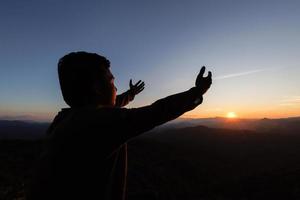 Silhouette eines Mannes, der die Hände mit dem Glauben an die Religion und den Glauben an Gott auf dem Hintergrund des morgendlichen Sonnenaufgangs betet. Gebetshaltung. foto