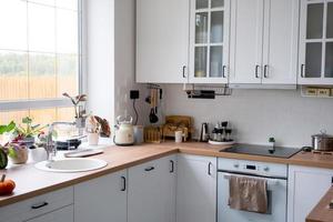 Weiße gemütliche Küche im Scandi-Loft-Stil. Inneneinrichtung, Esszimmerdesign, Backofen, Kochfeld, Tisch, Küchenmöbel foto