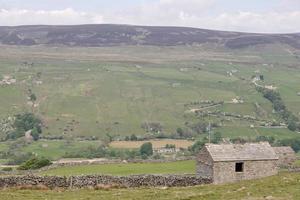 trockene gestapelte Steinmauer und Gebäude aus Stein mit einem bewölkten Himmel Yorkshire Dales United Kingdom foto