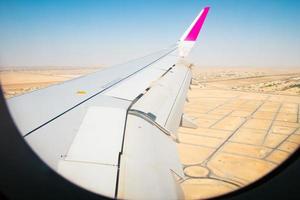 luftaufnahme über abu dhabi stadtvororte und wüste mit flügelhintergrundfenster. menschenleere landschaft der vae und flugzeugflügelansicht von der kabine. ferien urlaub im nahen osten konzept foto