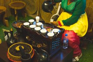 dubai, uae, 2022 - afrikanische dame gießt traditionellen kaffee aus dem topf in die tasse. alte Kaffeezubereitungsmethoden mit Vintage-Technologie