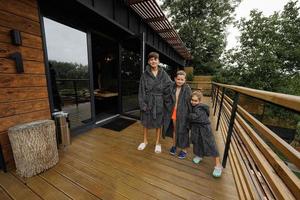 Drei Kinder im Bademantel stehen auf der Holzterrasse des modernen Hauses. foto