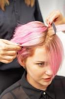 Friseur glättet rosa Haare der Frau durch Haareisen.