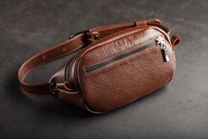 Eine braune Gürteltasche aus strukturiertem braunem Leder auf schwarzem Steinhintergrund. elegante Bauchtasche braune Tasche mit Reißverschluss foto