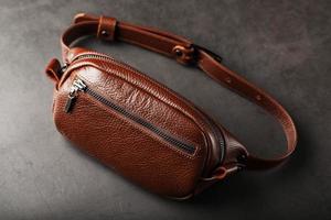 Eine braune Gürteltasche aus strukturiertem braunem Leder auf schwarzem Steinhintergrund. elegante Bauchtasche braune Tasche mit Reißverschluss foto