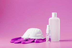 Stillleben mit Virenschutz auf rosa Hintergrund, Maske, Gummihandschuhen, einer Flasche Händedesinfektionsmittel, antiseptischem Gel. foto