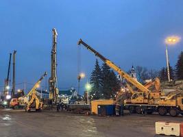 Baumaschinen an der Überführungsreparaturstelle. Ein großer, gelber Metallkran errichtet schwere Betonblöcke vor dem Hintergrund einer weißen Kuppelkirche foto