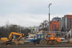 Viele leistungsstarke industrielle schwere spezialisierte Baumaschinen von Traktorbaggern und Bulldozern führen Straßenreparaturen während des Baus eines neuen Mikrobezirks in einer Großstadt durch foto