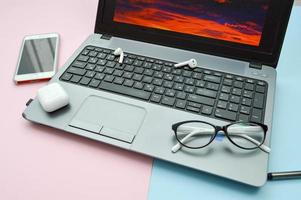 Arbeitsplatz zu Hause, Heimbüro für Fernarbeit mit einem Computer Laptop Handy Smartphone Notizblock Stift Kopfhörer und Brille auf rosa und blauem Hintergrund foto