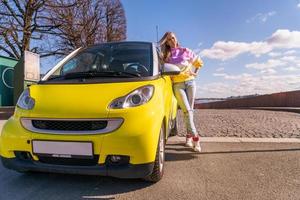 Schöne Frau, die an einem sonnigen Tag in der Nähe eines gelben Autos steht foto