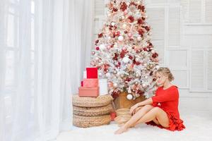 junge schöne frau sitzt auf dem boden in der nähe des weihnachtsbaums und präsentiert das neue jahr foto