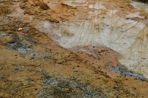 Textur einer schmutzigen, schlechten Schotterstraße Schotterstraße mit Pfützen und trocknendem Lehmschlamm mit Rissen und Furchen. Offroad. der Hintergrund foto