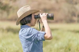 Frau trägt Hut und hält Fernglas auf der Wiese foto