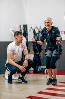 ältere frau, die ems-training mit trainer im fitnessstudio macht foto