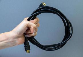 weibliche hand, die hdmi-kabel auf grauem hintergrund lokalisiert hält foto