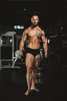 Mann trainiert mit Gewichten und zeigt seine Muskeln im Fitnessstudio foto