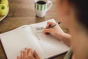 Frau, die eine To-Do-Liste macht, während sie den Morgenkaffee zu Hause genießt foto