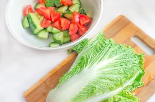 Chinakohl und Gemüsesalat auf Holzbrett. Gemüse auf weißem Tisch. gesundes vegetarisches essen. frisches Gemüse. Diät-Konzept. einfacher vegetarischer salat. einen einfachen Salat kochen. foto