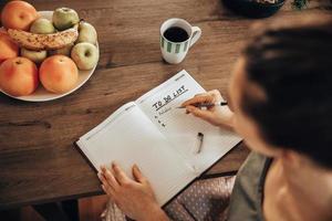 Frau, die eine To-Do-Liste macht, während sie den Morgenkaffee zu Hause genießt foto