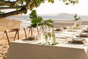 Schöner Tisch für ein romantisches Abendessen am Strand mit Blumen und Kerzen. Catering für ein romantisches Date, eine Hochzeit oder einen Flitterwochenhintergrund. Abendessen am Strand bei Sonnenuntergang. ausgewählten Fokus. foto