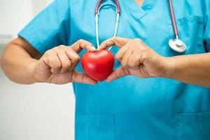 Arzt, der ein rotes Herz in der Krankenstation hält, gesundes, starkes medizinisches Konzept.