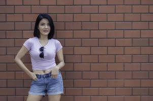 Porträt eines Hipster-Mädchens auf Backsteinmauerhintergrund, schöne asiatische Frauenpose für ein Foto
