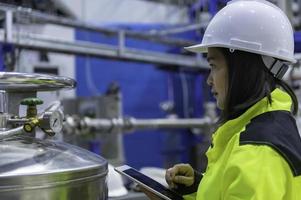 asiatischer ingenieur, der in der betriebshalle arbeitet, thailänder tragen helmarbeiten, er arbeitete mit fleiß und geduldig, sie überprüfte den ventilregler am wasserstofftank. foto