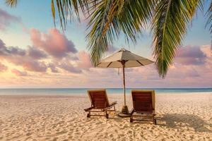 erstaunlicher Strand bei Sonnenuntergang. romantisches Paar Stühle Regenschirm. ruhige zusammengehörigkeit liebe konzept landschaft, relax strand, schöne landschaftsgestaltung. Kurzurlaub tropisches Inselufer, Palmenblätter, idyllischer Meerblick foto