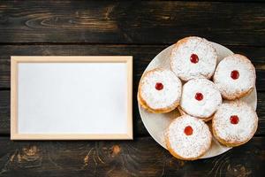 Fröhliches Hanukkah. leerer rahmen für glückwunschtext und traditionelles dessert sufganiyot auf dunklem holzhintergrund. jüdischen Feiertag feiern. foto