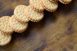 Ein runder Sandwichkeks mit Kokosfüllung liegt in großen Mengen auf einer braunen Holzoberfläche. Foto von essbaren Leckereien auf einem hölzernen Hintergrund mit Kopierraum