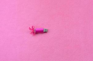 Eine leuchtend rosa USB-Flash-Speicherkarte mit einer rosa Schleife liegt auf einer Decke aus weichem und pelzigem hellrosa Fleece-Stoff. klassisches weibliches Geschenkdesign für eine Speicherkarte foto