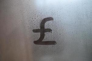 Symbol des englischen Pfunds wird mit einem Finger auf die Oberfläche des beschlagenen Glases geschrieben foto