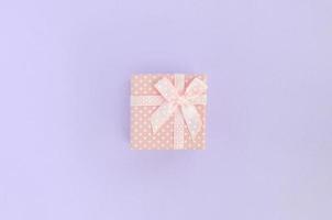 kleine rosa geschenkbox mit band liegt auf violettem hintergrund. minimalismus flach draufsicht foto