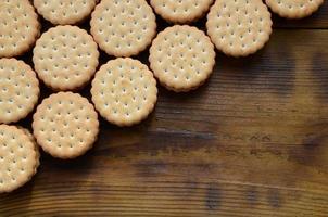 Ein runder Sandwichkeks mit Kokosfüllung liegt in großen Mengen auf einer braunen Holzoberfläche. Foto von essbaren Leckereien auf einem hölzernen Hintergrund mit Kopierraum