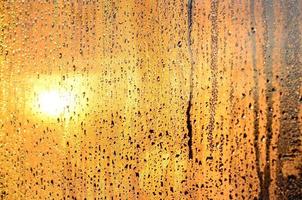 die textur von beschlagenem glas mit vielen tropfen und tropfen von kondenswasser gegen das sonnenlicht im morgengrauen. Hintergrundbild foto