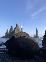 Mann steht auf einem Felsen am schwarzen Strand von Reynisfjara, Island, mit Wind im Haar foto