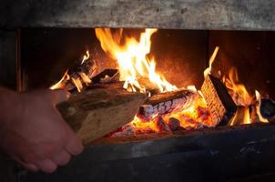 Hand legt ein Holzscheit auf ein Feuer, um ein Haus zu heizen foto