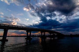 das Bild schöner Regenwolken, die sich über der Brücke über dem Fluss in Bewegung sammelten foto