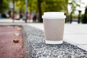 Einwegkaffeetasse auf Bürgersteig mit Stadt im Hintergrund