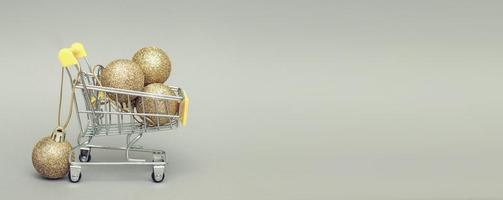 Einkaufswagen mit glänzenden goldenen Weihnachtsspielzeugkugeln auf grauem Hintergrund. Banner foto