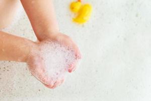 Kleines Mädchen, das mit Schaum in einer Badewanne spielt. Kind spielt mit Spielzeug im Badezimmer. foto