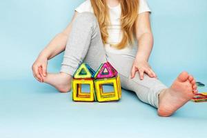 Kleines Mädchen, das mit buntem magnetischem Konstruktorspielzeug auf blauem Hintergrund spielt. Kind hat ein Haus gebaut foto