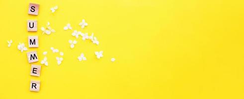 Wort Sommer geschrieben von Holzwürfeln mit Buchstaben auf gelbem Hintergrund mit Blütenblättern einer Hortensie foto