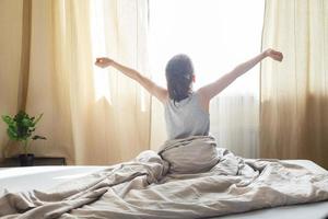 kleiner Junge sitzt und streckt sich morgens zu Hause im Bett auf einem Fensterhintergrund foto