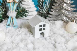 abstrakter Adventsweihnachtshintergrund. Spielzeugmodellhaus und Winterdekorationsverzierungen auf blauem Hintergrund mit Schnee. weihnachten mit familienkonzept zu hause. foto